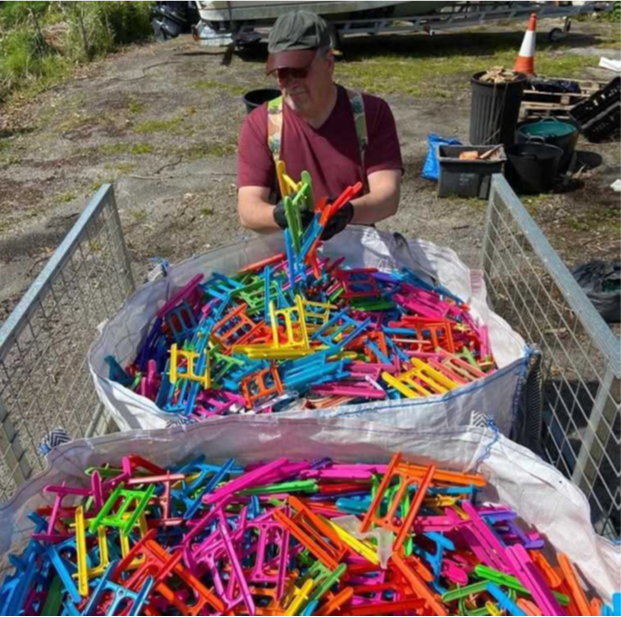 A volunteer dressed in a green cap and red t-shirt stands behind a two large white sacks full of colourful plastic crab line reels. He is adding more reels. The sacks stand between two metal grilles.