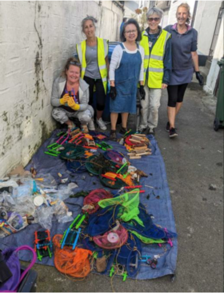 Five smiling Looe Marine Conservation Group volunteers pose behind the collected and sorted crab line recycling materials, arranged on a blue mat.